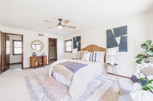 bedroom with visible vents, a walk in closet, baseboards, light colored carpet, and ceiling fan