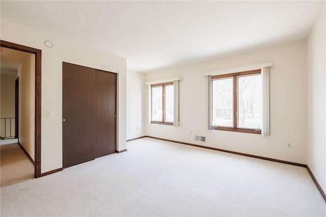 unfurnished bedroom featuring visible vents, baseboards, light colored carpet, and a closet