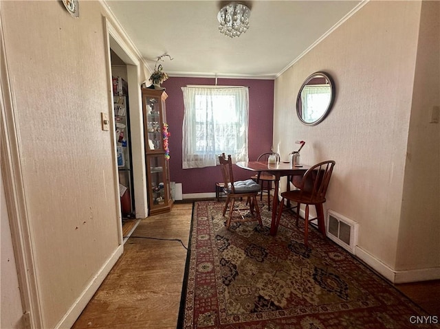 dining room with crown molding, wood finished floors, visible vents, and baseboards