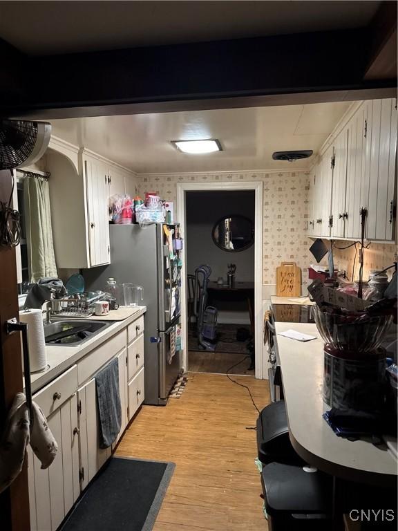 kitchen featuring a sink, wallpapered walls, freestanding refrigerator, light wood finished floors, and light countertops