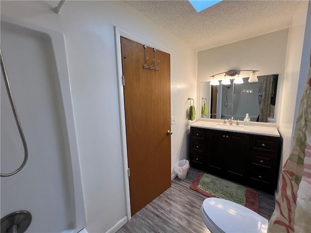 full bath featuring vanity, wood finished floors, a skylight, a textured ceiling, and toilet