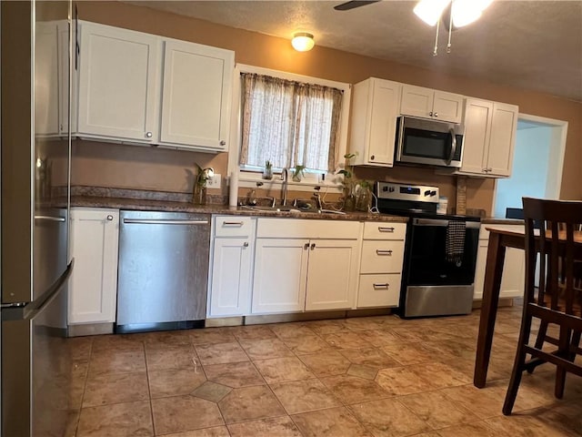 kitchen with a sink, stainless steel appliances, dark countertops, and white cabinets