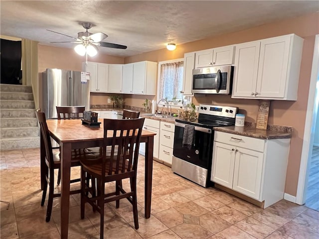 kitchen with baseboards, ceiling fan, a sink, white cabinets, and appliances with stainless steel finishes