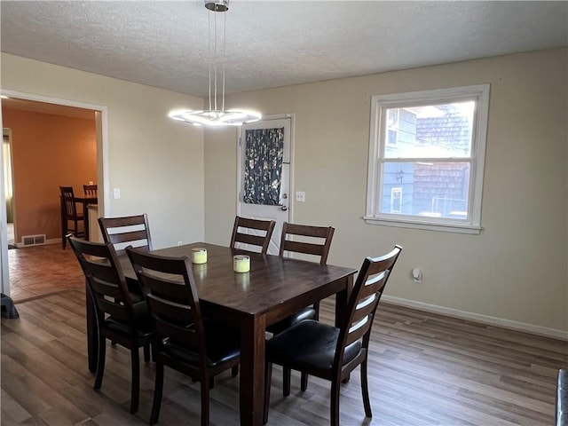 dining area with visible vents, baseboards, a textured ceiling, and wood finished floors