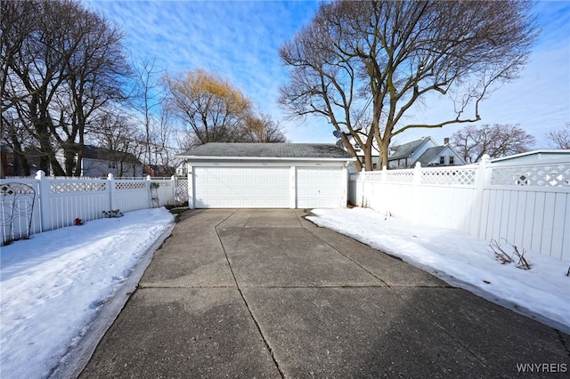 snow covered garage featuring a detached garage and fence