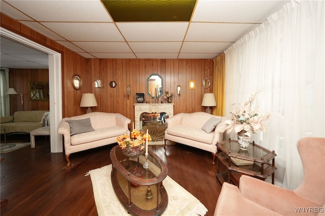 living room with dark wood-type flooring, a fireplace, wood walls, and a drop ceiling