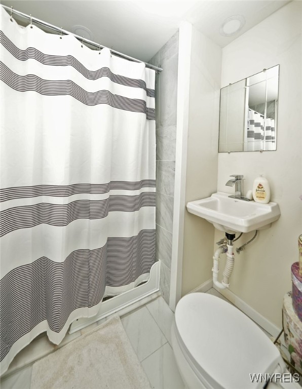 bathroom with marble finish floor, toilet, a shower with shower curtain, and a sink