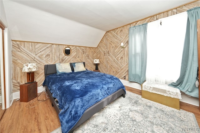 bedroom featuring wood finished floors, wood walls, and vaulted ceiling