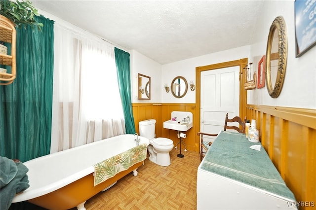 bathroom featuring a wainscoted wall, a textured ceiling, a soaking tub, and toilet