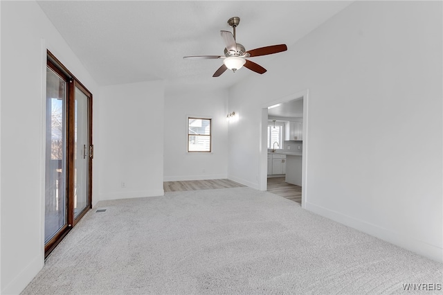 unfurnished living room with a sink, light colored carpet, baseboards, and ceiling fan