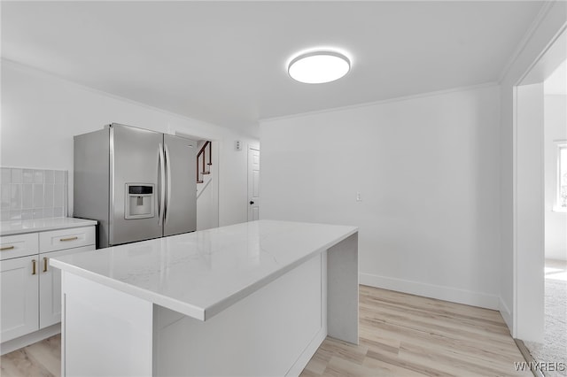 kitchen featuring light stone countertops, light wood-type flooring, ornamental molding, white cabinets, and stainless steel fridge