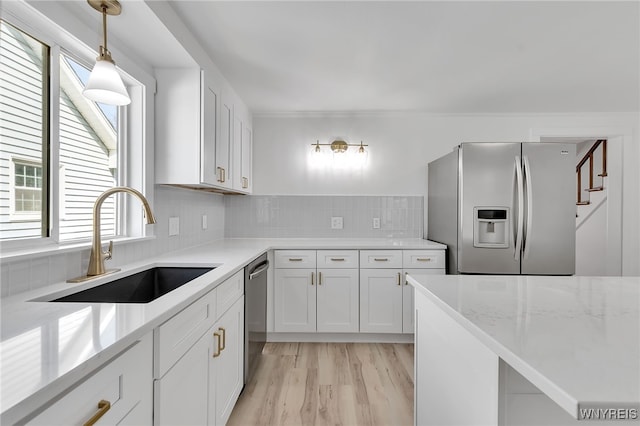 kitchen featuring light wood-type flooring, a sink, decorative light fixtures, appliances with stainless steel finishes, and white cabinets