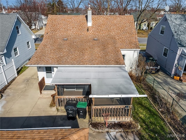 back of house featuring a residential view, fence, a chimney, and a shingled roof