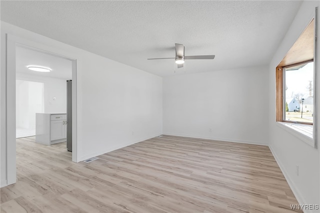 spare room featuring light wood finished floors, visible vents, baseboards, ceiling fan, and a textured ceiling