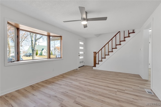 interior space featuring visible vents, a textured ceiling, wood finished floors, stairway, and ceiling fan