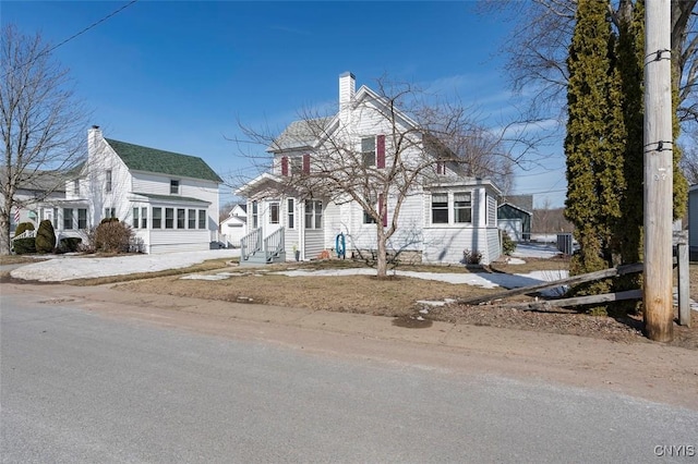 view of front facade with entry steps, a chimney, and a sunroom