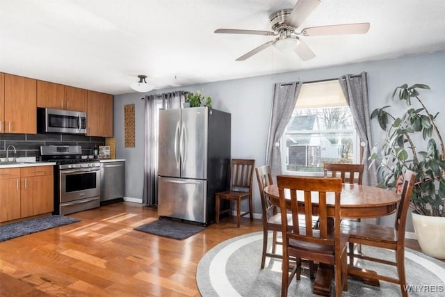 kitchen featuring a sink, stainless steel appliances, light wood-style floors, brown cabinetry, and light countertops