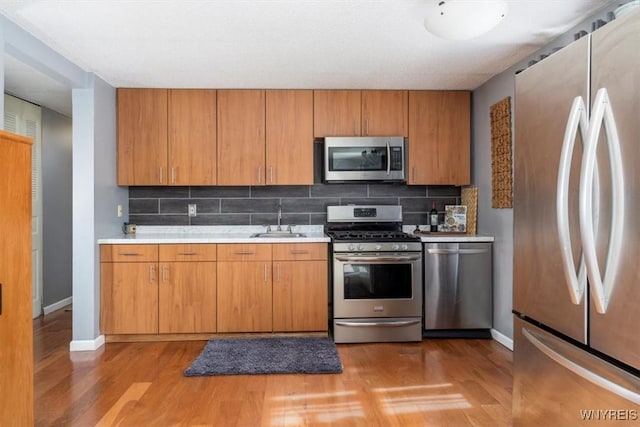 kitchen with light wood-style flooring, a sink, stainless steel appliances, brown cabinetry, and light countertops