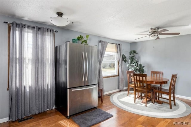 dining space with baseboards, a textured ceiling, light wood-type flooring, and ceiling fan