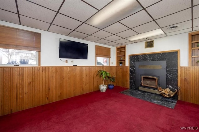 carpeted living room featuring wooden walls, built in features, visible vents, a wainscoted wall, and a premium fireplace