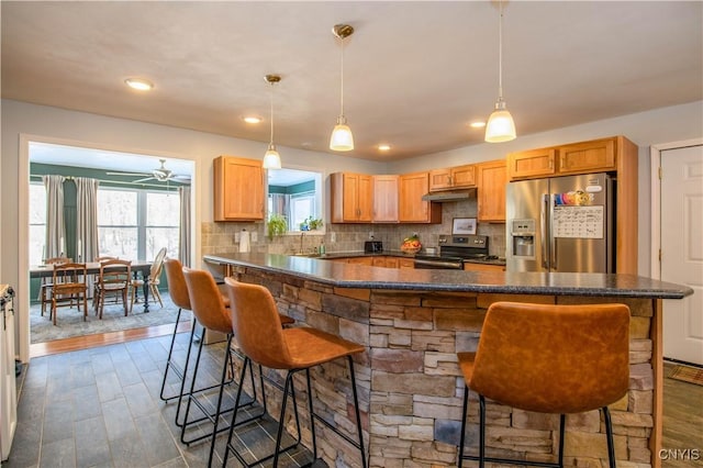 kitchen featuring under cabinet range hood, stainless steel appliances, a kitchen bar, and tasteful backsplash