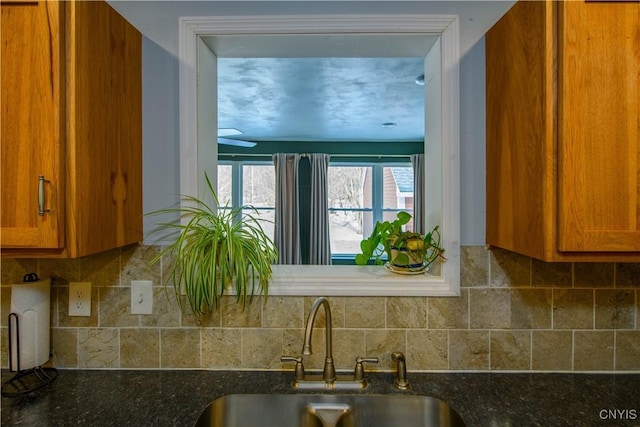 kitchen featuring brown cabinetry, dark stone countertops, backsplash, and a sink