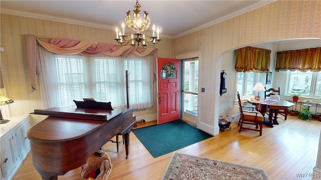 foyer entrance with wallpapered walls, light wood-type flooring, ornamental molding, an inviting chandelier, and arched walkways