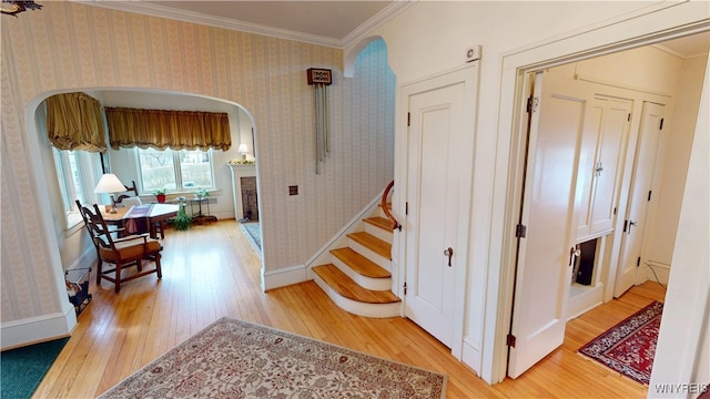 stairs featuring arched walkways, ornamental molding, wallpapered walls, and hardwood / wood-style floors