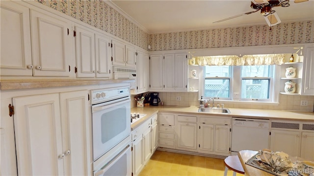 kitchen with a ceiling fan, a sink, wallpapered walls, white appliances, and light countertops