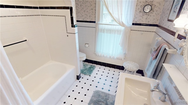 bathroom with wallpapered walls, tile walls, toilet, and a wainscoted wall