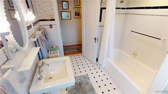 bathroom with wallpapered walls, wainscoting, tile patterned floors, tile walls, and a sink