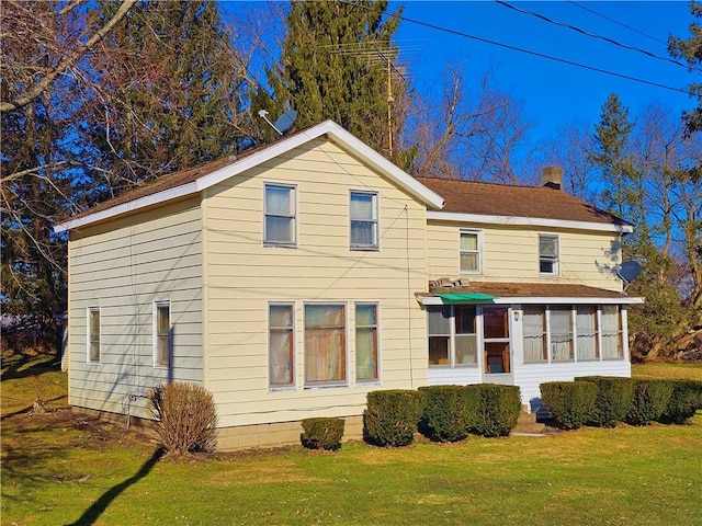 rear view of property featuring a lawn, a sunroom, and a chimney