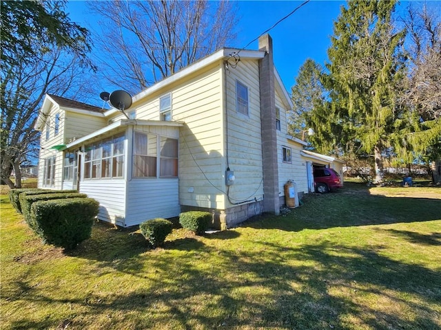 view of side of home featuring a lawn, a chimney, and a sunroom