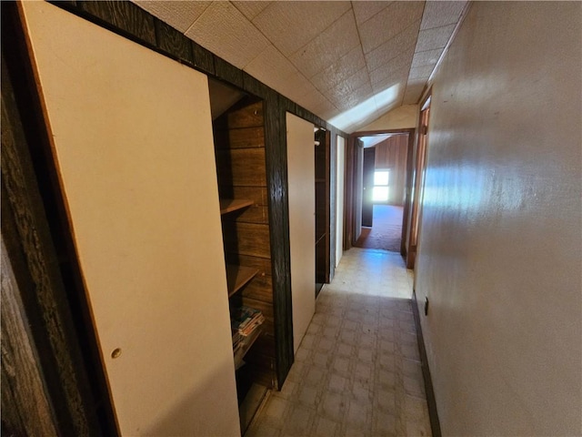 corridor featuring light floors, wood walls, and lofted ceiling