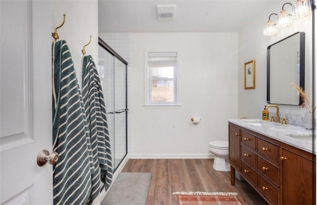 full bathroom with toilet, double vanity, a stall shower, wood finished floors, and a sink