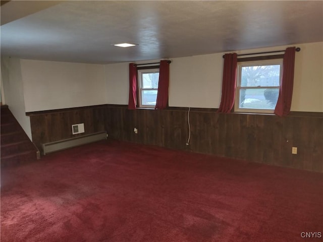 unfurnished room with baseboard heating, wood walls, carpet, and a wainscoted wall