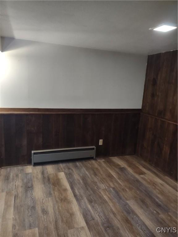 unfurnished room featuring a baseboard radiator, wood finished floors, wainscoting, and wood walls