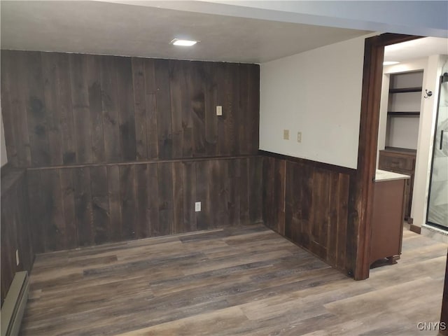 empty room featuring wooden walls, a baseboard heating unit, and wood finished floors