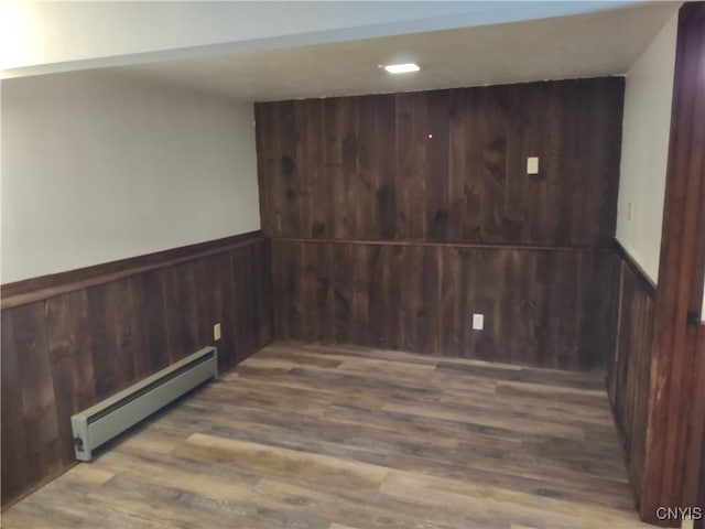 empty room with a baseboard radiator, wood finished floors, wood walls, and wainscoting