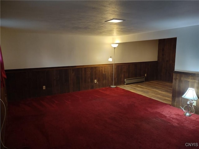 finished basement featuring a textured ceiling, carpet floors, wooden walls, wainscoting, and a baseboard radiator