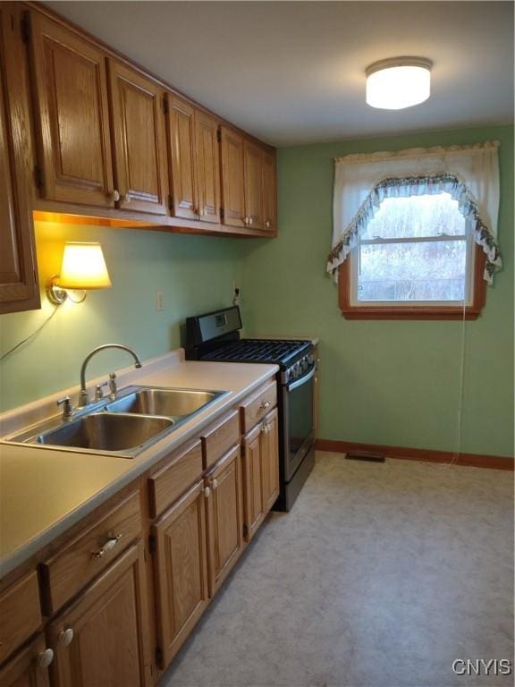 kitchen with a sink, brown cabinetry, stainless steel gas range, and light countertops