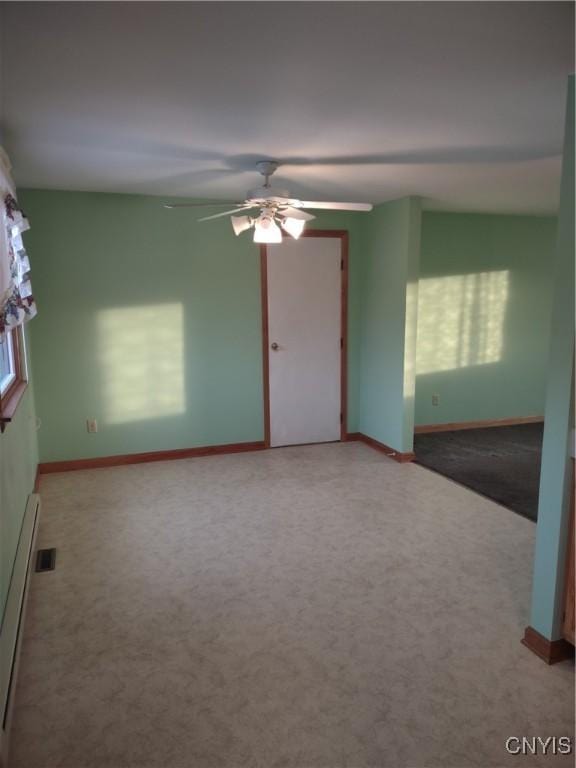 carpeted empty room with a wealth of natural light, visible vents, a baseboard radiator, baseboards, and ceiling fan