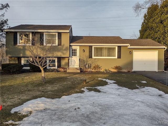 tri-level home with an attached garage, driveway, and roof with shingles