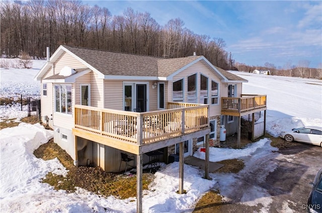 snow covered rear of property featuring a shingled roof and a deck