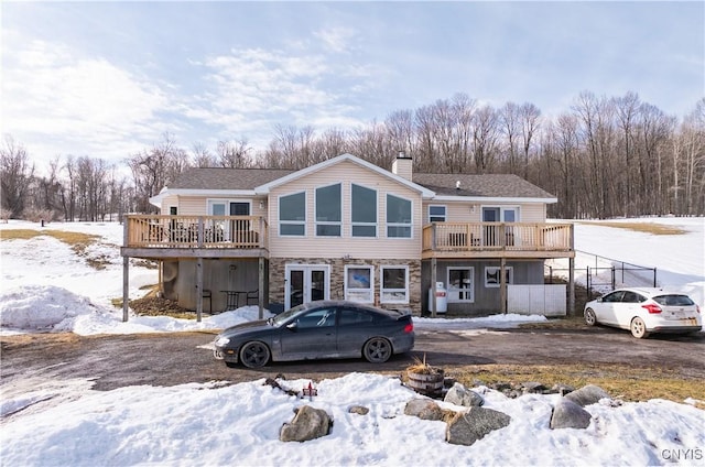 snow covered house with a chimney, stone siding, and a wooden deck