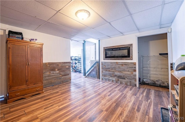 unfurnished living room with a paneled ceiling, wooden walls, and wood finished floors