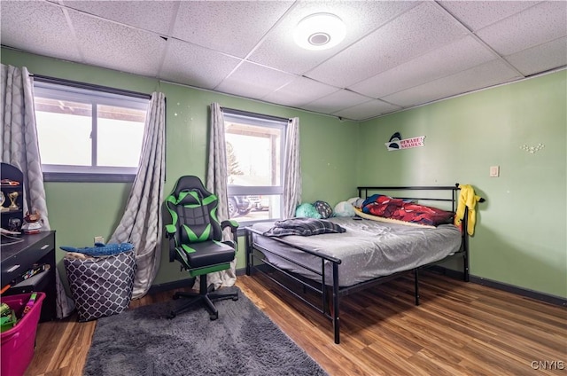 bedroom featuring a drop ceiling, baseboards, and wood finished floors