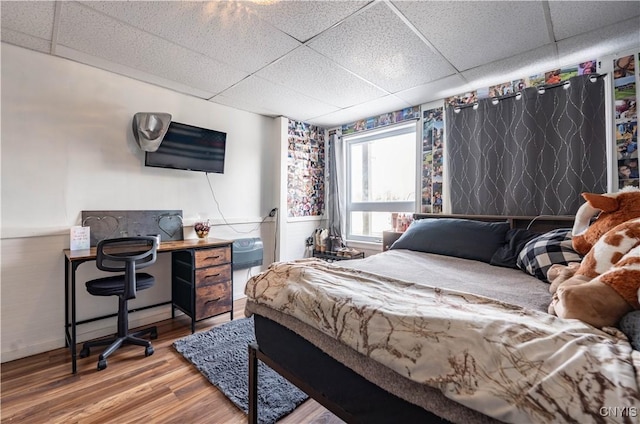 bedroom featuring a drop ceiling, wood finished floors, and wainscoting