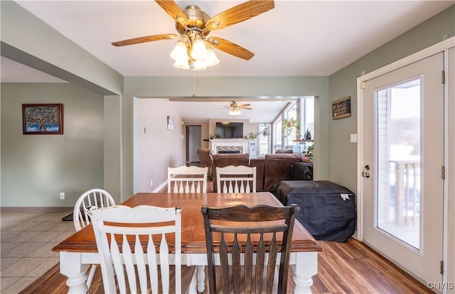 dining room with tile patterned floors, baseboards, a ceiling fan, and a fireplace