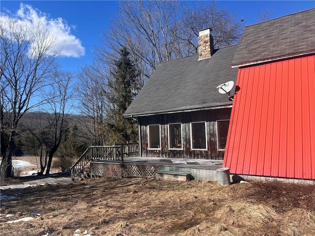 rear view of house featuring roof with shingles, a deck, and a chimney